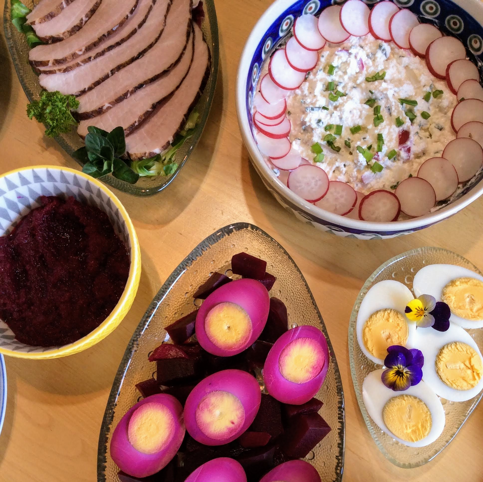 A plate of slice meat, a bowl of radish and cheese salad, a plate of hard-boiled eggs, a plate of pickled eggs, a bowl of beet and horseradish relish for Easter.