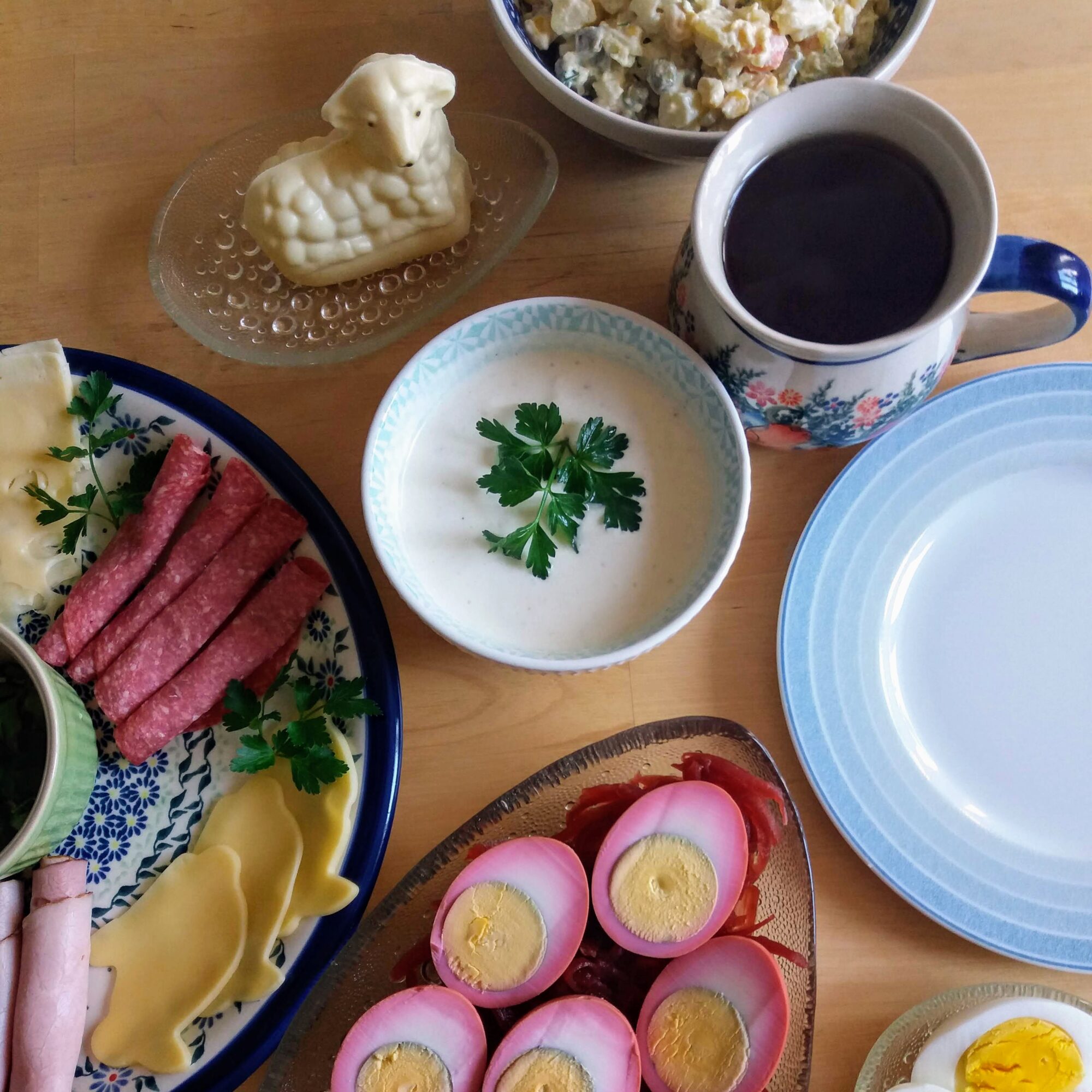 A plate of cheese and meat with a bowl of horseradish sauce, pickled eggs, a cup of tea, and a butter lamb.