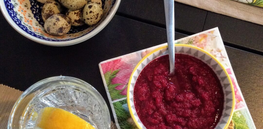 A bowl of beet and horseradish relish with a bowl of quail eggs and a glass of water with lemon.