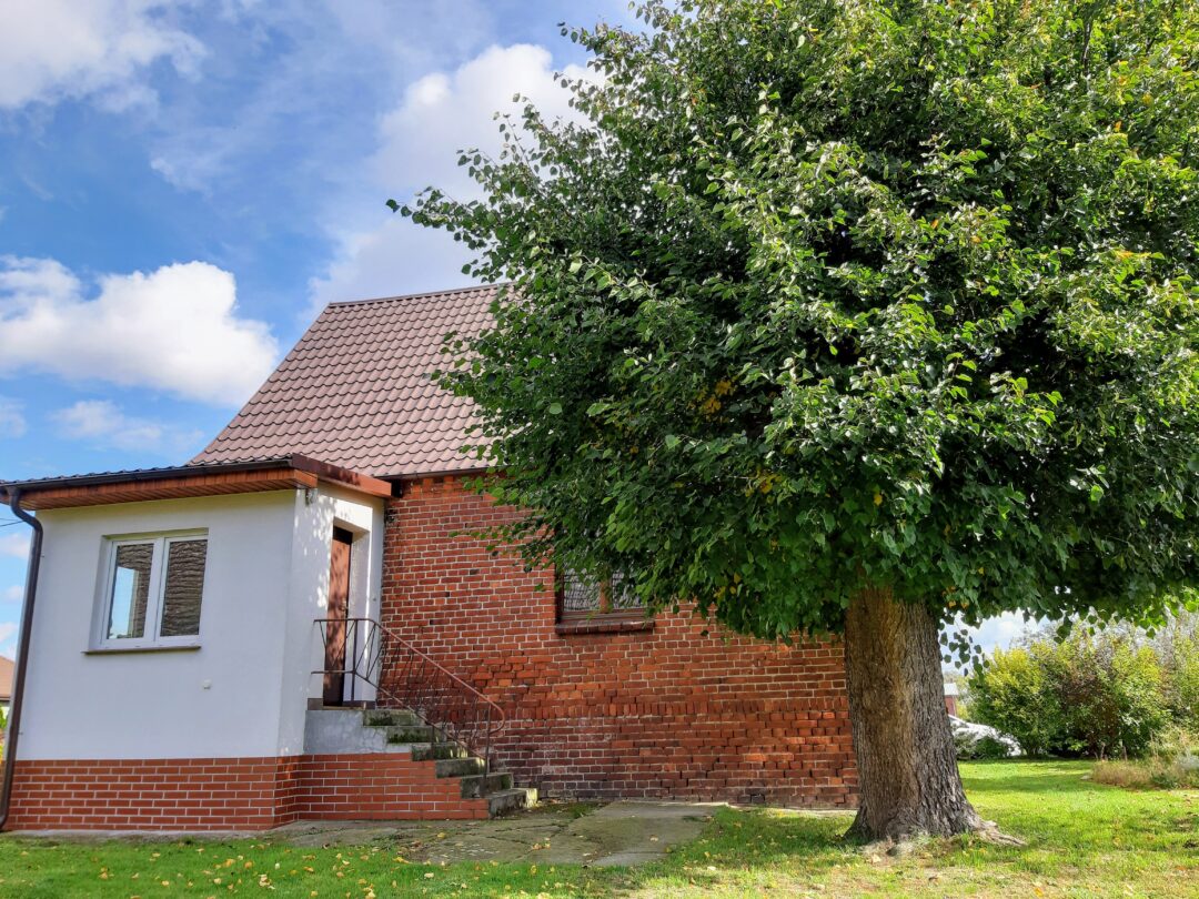 A red brick farmhouse in German style with a white added-on porch and a linden tree
