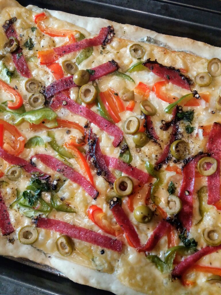 Pizza topped with peppers, salami strips and olives