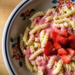 A plate of macaroni topped with a strawberry cream sauce and chopped strawberries