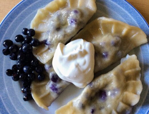 Plate of blueberry pierogi with a dollop of cream in the middle and blueberries on the left side